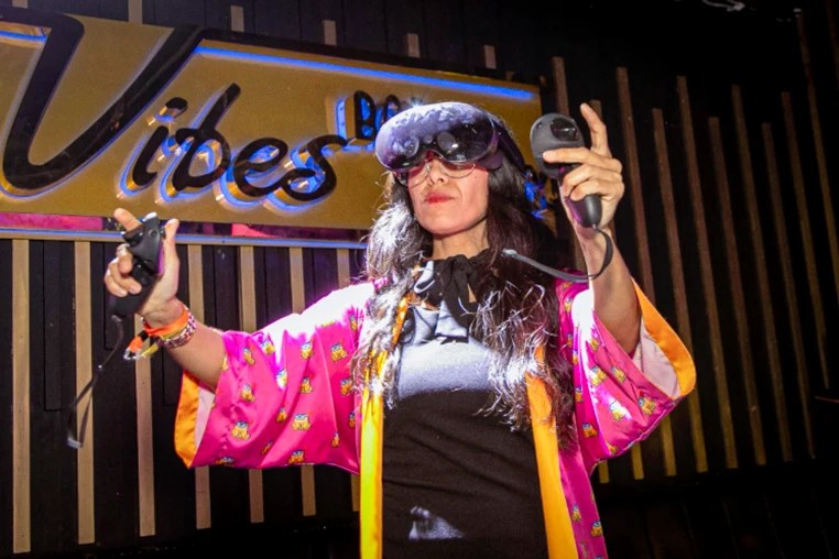 Creatress in a pink kimono and mixed reality headset under a neon Vibes sign