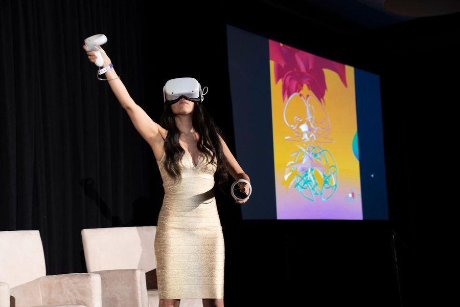 Creatress reaching up with a controller while a colorful sculpture shows on screen